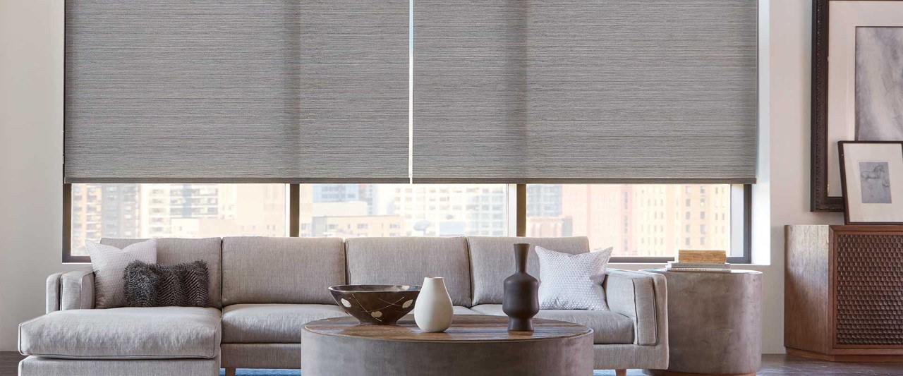 Circular coffee table with large grey couch and windows looking out to the city.